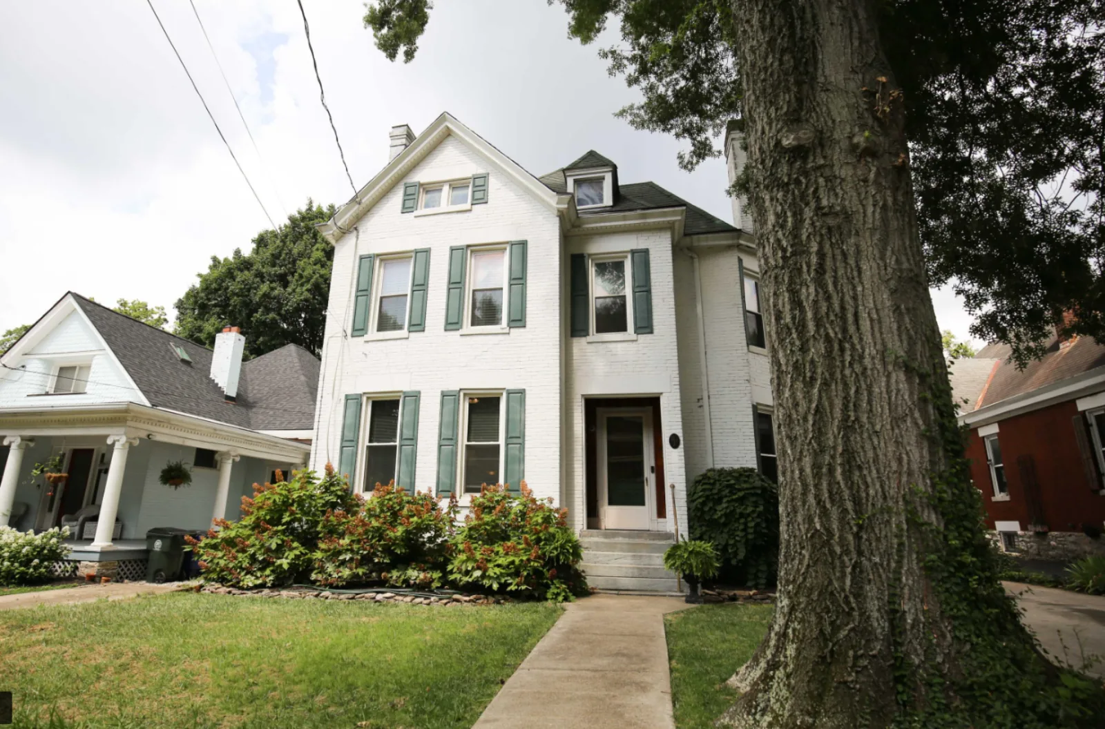 White two-story historic home with green shutters on a tree-lined street near downtown Lexington