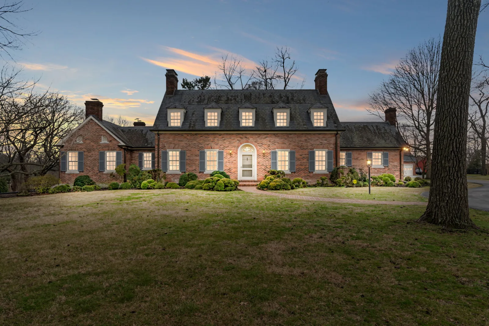 A stately brick Colonial home with manicured landscaping at dusk in Lexington KY
