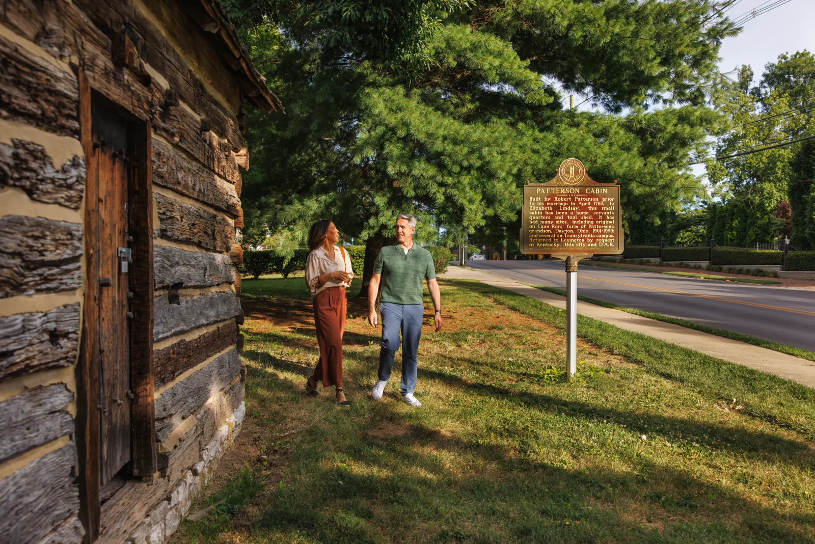 A couple walking past the historic Patterson log cabin at Royal Spring Park in Georgetown KY